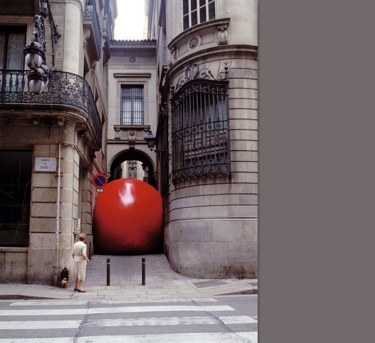 woman looking at a giant red ball trapped in an alley between two buildings.